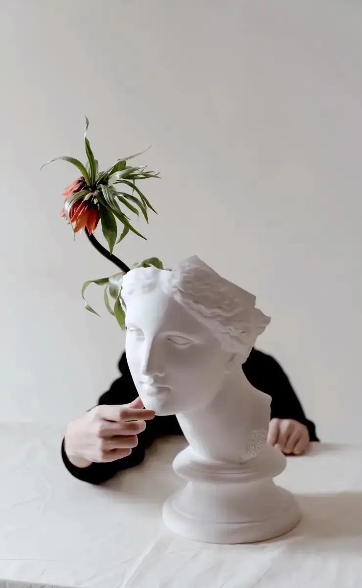 Person arranging flowers in a white vase shaped like a classical bust